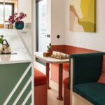 Jedálenský kút s tehlovočervenou čalúnenou lavicou, svetlým dreveným stolom a farebným abstraktným obrazom.