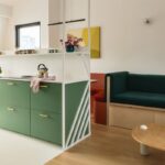 Moderná zelená kuchynská linka, prepojená s obývacou časťou a dreveným stolíkom.