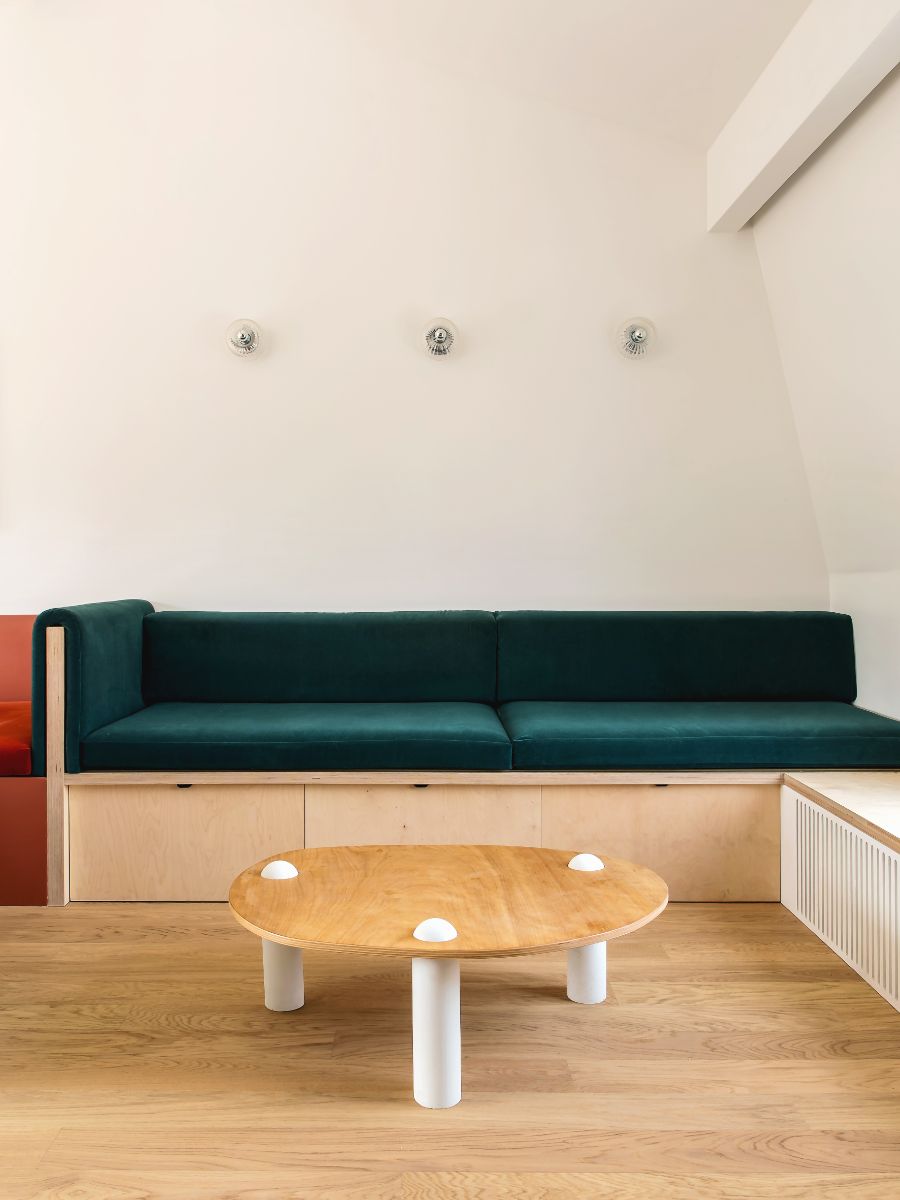 Tmavozelená zamatová sedačka s konštrukciou svetlej preglejky zo pred bielou stenou