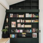 Vysoká čierna policová knižnica so šikmým horným ukončením a farebnými knihami