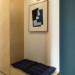 reglejková lavica s modrými vankúšmi pod moderným abstraktným obrazom.