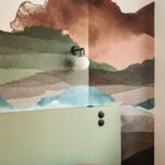 Farebná tapeta s motívom hôr nad zeleným čelom postele.