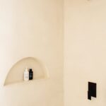 Minimalistický béžový sprchový kút s čiernou štvorcovou hlavicou a oblúkovou nikou.