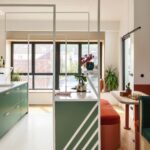 Zelená kuchynská skrinka so zelenými čelami a bielou pracovnou doskou, za ktorou je jedálenský kút s červenou lavičkou a dreveným stolom.