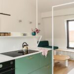 Zelená kuchynská linka s čiernou rúrou, bielou pracovnou doskou a okrúhlym dreveným stolíkom pri okne.