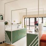 Kuchynská zóna so zelenými skrinkami, bielou kovovou konštrukciou a veľkým oknom s výhľadom na mesto.