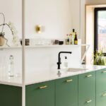 Zelená kuchynská linka s bielou kamennou doskou a čiernou vodovodnou batériou.