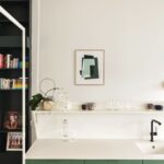 Kuchynská linka so zelenými skrinkami otvorenou bielou policou a obrazom na stene.