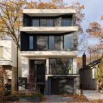 Predná fasáda úzkeho mestského domu s tmavou vertikálnou fasádou, svetlými balkónovými líniami a integrovanou garážou.