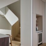 Béžová nábytková zostava so zabudovanou vinotékou vedľa masívneho dreveného schodiska s plnou bočnicou.