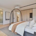 Spálňa s posteľou s kovovou konštrukciou, svetlou šatníkovou skriňou a vstupom do kúpeľne.