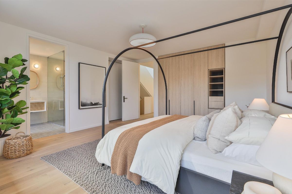 Spálňa s posteľou s kovovou konštrukciou, svetlou šatníkovou skriňou a vstupom do kúpeľne.