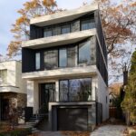 Moderná trojpodlažná mestská vila s čiernym dreveným obkladom, bielymi betónovými rímsami a veľkými presklenými plochami.