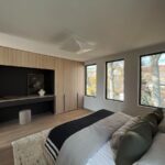 Moderná spálňa s čalúnenou posteľou oproti drevenej nábytkovej stene s nikou pod tromi vertikálnymi oknami.