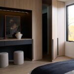 Drevená šatníková zostava s otvoreným krídlom vedľa čiernej toaletnej konzoly s bielymi taburetkami na koberci.