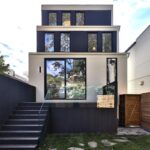 Zadná fasáda terasovitého domu s krémovou omietkou, čiernym dreveným latovaním a skleneným zábradlím na vyvýšenej terase.