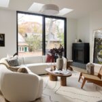 Svetlá obývacia izba s bielou oblou pohovkou, dreveným konferenčným stolíkom a čiernym moderným krbom pri veľkom okne.