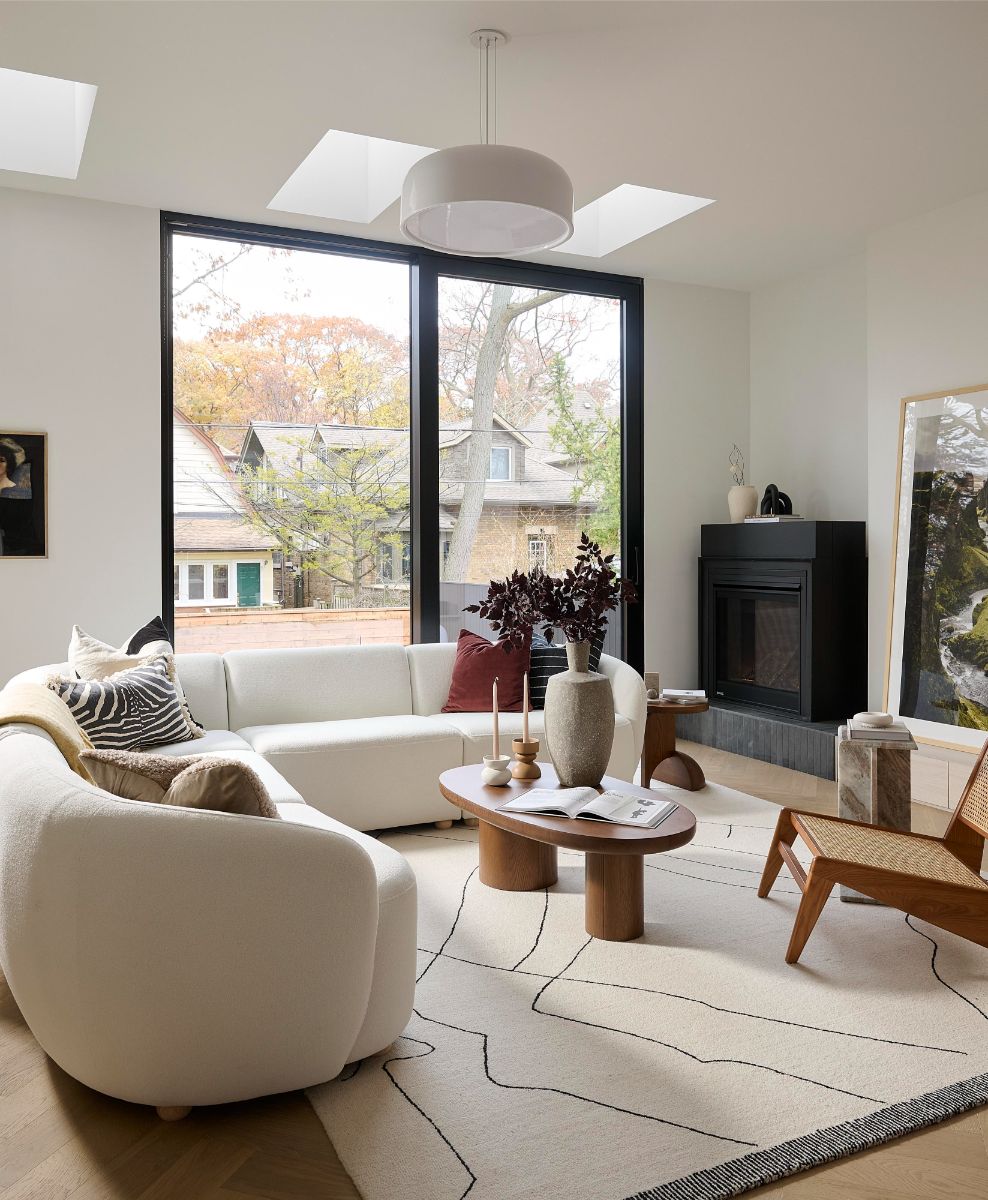 Svetlá obývacia izba s bielou oblou pohovkou, dreveným konferenčným stolíkom a čiernym moderným krbom pri veľkom okne.