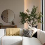 Biela štruktúrovaná sedačka s čiernobielou vzorovanou poduškou a živý olivovník pred minimalistickou béžovou stenou.