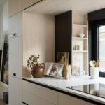 Svetlá kuchynská linka s béžovými skrinkami, hlineným hnedým džbánom a otvorenými policami z bledého dreva.