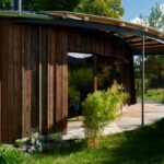 Exteriér moderného drevodomu s oblými líniami a drevenou terasou.