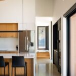 Svetlá kuchyňa s dreveným stropom, nerezovou chladničkou, bielou pracovnou doskou a čiernymi koženými stoličkami.