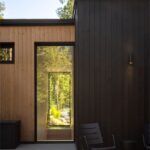Tmavá drevená fasáda s presklenými dverami s výhľadom na zelené stromy.