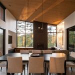 Čierny jedálenský stôl s béžovými stoličkami, dizajnový luster, tmavý krb a drevený strop v otvorenom priestore.