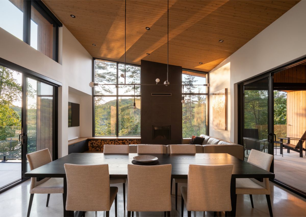 Čierny jedálenský stôl s béžovými stoličkami, dizajnový luster, tmavý krb a drevený strop v otvorenom priestore.