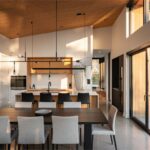 Otvorený interiér s modernou vstavanou kuchyňou s kuchynským ostrovom, čiernymi stoličkami, jedálenským stolom a posuvnými dverami na terasu.