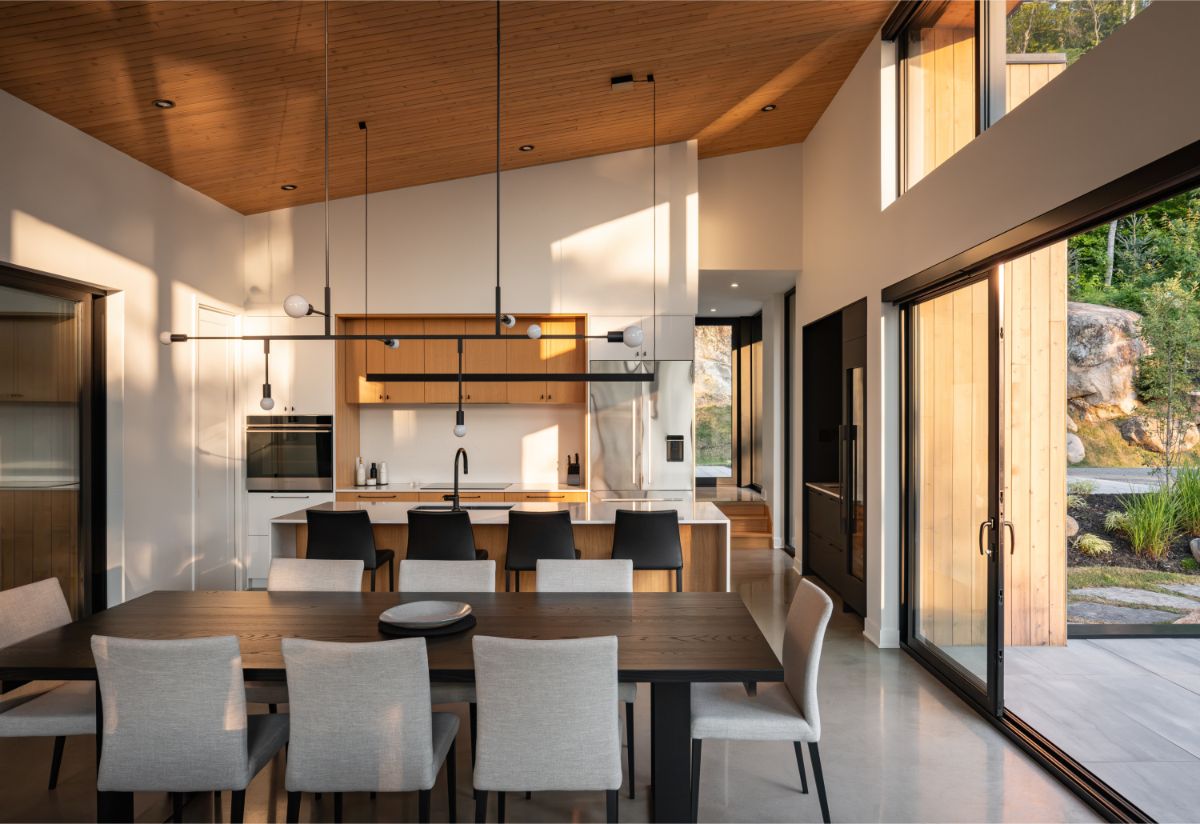 Otvorený interiér s modernou vstavanou kuchyňou s kuchynským ostrovom, čiernymi stoličkami, jedálenským stolom a posuvnými dverami na terasu.