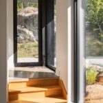 Presvetlená chodba s betónovou podlahou, drevenými schodmi, a oknami s čiernymi rámami.