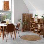 Biely okrúhly stôl, hnedé koženkové stoličky, drevený policový regál a pletené bambusové svietidlo.