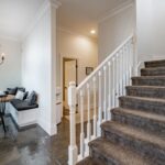 Drevený okrúhly stôl, čierna latková stolička, biela rohová lavica a schodisko s hnedým kobercom.