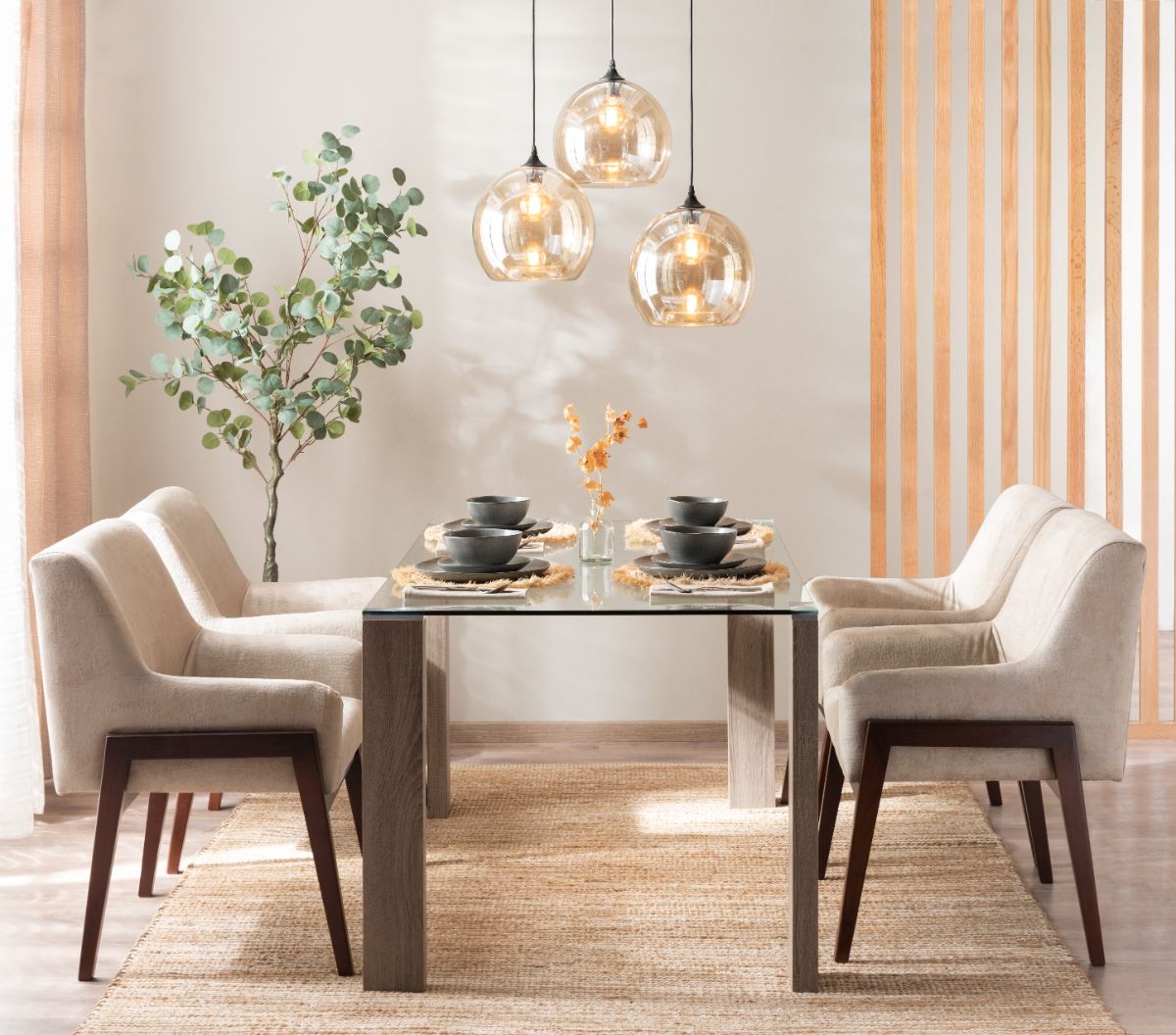 Sklenený jedálenský stôl, béžové čalúnené kreslá, tri sklenené lustre a vysoký zelený fikus.
