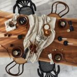 Rustikálny stôl z tmavého dreva, čierne prútené stoličky a svetlá keramická súprava na ľanovom obruse.