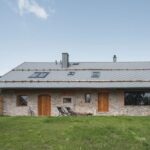 Kamenná chalupa s drevenými oknami a dvorom.