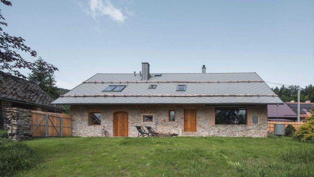 Kamenná chalupa s drevenými oknami a dvorom.