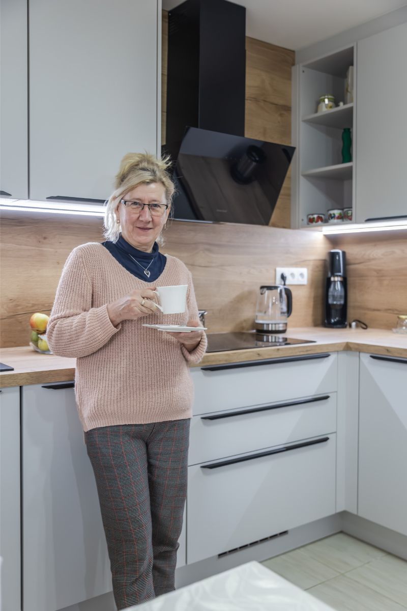 Žena v bielej kuchyni s dubovou pracovnou doskou, čiernou varnou doskou a moderným sodastreamom v rohu linky.