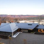 Fasáda moderného domu so šedou plechovou strechou a kameňom, zasadeného do prírody s výhľadom na jazero.