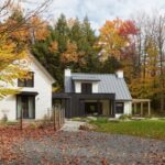 Moderný biely dom s čiernymi a drevenými prvkami v lese.