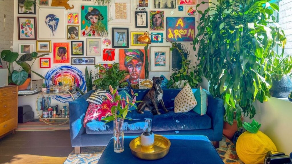 Interiér s množstvom farebných obrazov, sýtomodrou pohovkou, rastlinami a farebnými vankúšmi.