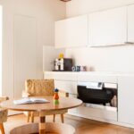 Kuchynský kút s bielymi skrinkami, okrúhlym dreveným stolíkom a vzorovaným kreslom v retro štýle.