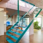 Moderné tyrkysové oceľové schodisko so sklenenými stupňami umiestnené pred zrkadlovou stenou v otvorenom lofte.