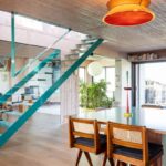 Jedálenský kút s drevenými stoličkami, tyrkysovým schodiskom v pozadí a výrazným oranžovým stropným svietidlom.
