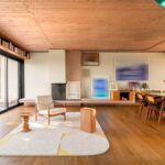 Priestranná obývacia izba s masívnym jedálenským stolom, dizajnovým kreslom, drevenými parketami a nástennou knižnicou.