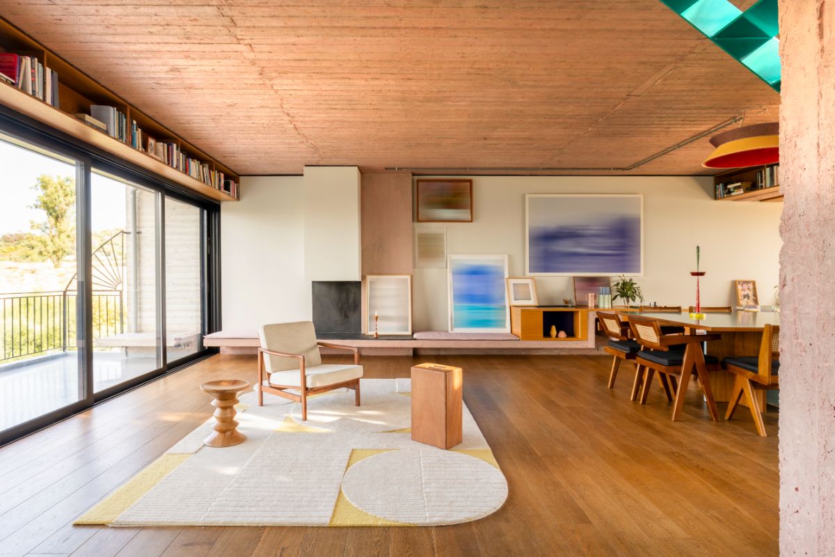 Priestranná obývacia izba s masívnym jedálenským stolom, dizajnovým kreslom, drevenými parketami a nástennou knižnicou.