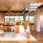 Moderný otvorený priestor s tyrkysovým oceľovým schodiskom, dreveným nábytkom a ružovým betónovým nosným stĺpom.