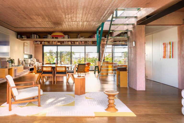 Moderný otvorený priestor s tyrkysovým oceľovým schodiskom, dreveným nábytkom a ružovým betónovým nosným stĺpom.