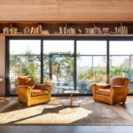 Dve kožené kreslá v koňakovej farbe na orientálnom koberci pred veľkým preskleným portálom s výhľadom na terasu.